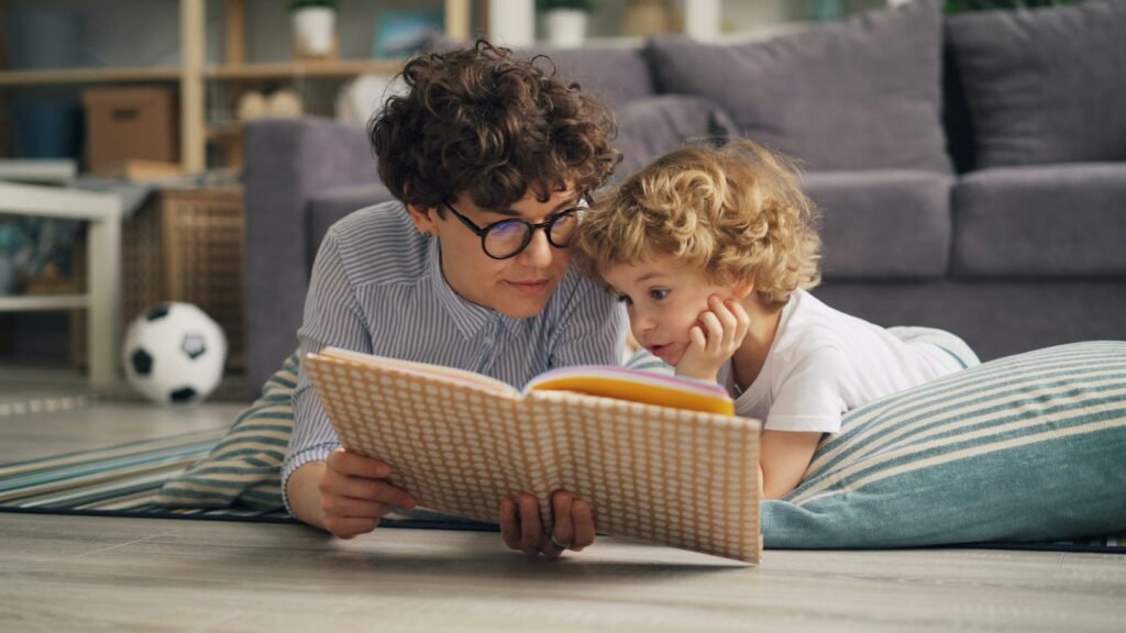 A mother and child lying on the floor reading a book together at home